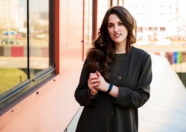 Şık, mutlu, uzun, güzel saçlı, takım elbiseli güzel bir kadının fotoğrafı. Güneşli bir havada binanın arka planında.