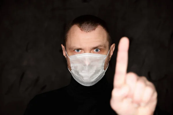 Portrait of a man in a medical mask shows his fingers on a black background