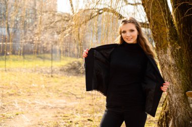 Parkta ahşap bir arka planda gülüşü olan, uzun saçlı, zarif bir genç kızın bahar portresi. Fotoğraf açık havada güneşli bir havada çekildi..