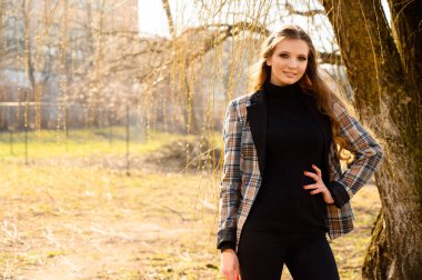 Parkta ahşap bir arka planda gülüşü olan, uzun saçlı, zarif bir genç kızın bahar portresi. Fotoğraf açık havada güneşli bir havada çekildi..