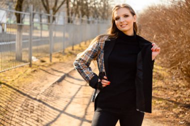 Tarz sahibi, güzel bir genç kızın portresi. Uzun saçlı, parkın arka planında gülümsemesi olan. Fotoğraf, baharda açık havada güneşli bir havada çekildi..