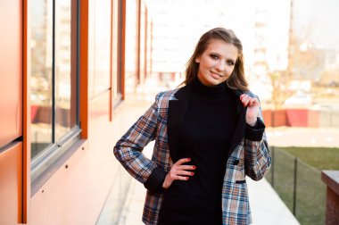 Uzun saçlı, güzel bir genç kızın portresi. Parkta bir binanın arka planında gülümsüyor. Fotoğraf, baharda açık havada güneşli bir havada çekildi..