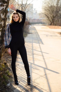 Uzun saçlı, kentte gülümseyen ve pencereli bir iş binasının duvarına dayanan zarif bir genç kadının tam boy portresi. Baharda güneşli ve açık havada çekilmiş bir fotoğraf..