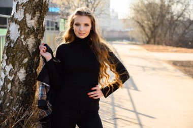 Uzun saçlı, şık bir genç kadının portresi. Şehirde ahşap bir arka planda gülümsemesi var. Baharda güneşli ve açık havada çekilmiş bir fotoğraf..