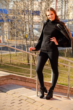 Şehrin arka planında uzun saçlı ve gülümseyen zarif bir genç kadının tam boy portresi. Baharda güneşli ve açık havada çekilmiş bir fotoğraf..