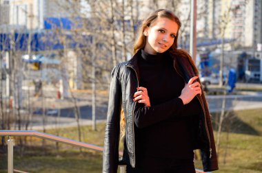 Şehrin arka planında gülümseyen uzun saçlı şık bir genç kadının portresi. Baharda güneşli ve açık havada çekilmiş bir fotoğraf..