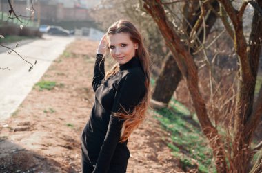 Parktaki yol ağaçlarının arka planında uzun saçlı güzel bir kızın portresi. Baharda güneşli ve açık havada çekilmiş bir fotoğraf..