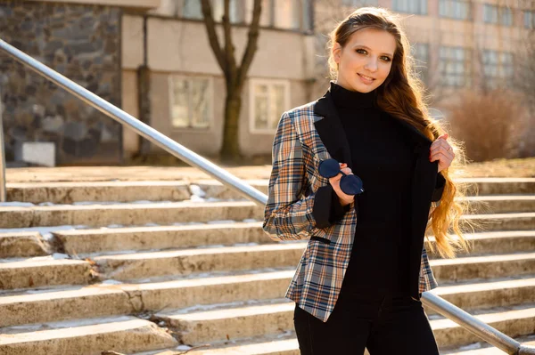 Şehrin arka planında, uzun saçlı ve gülümseyen güzel bir genç kızın bahar portresi. Fotoğraf açık havada güneşli bir havada çekildi..