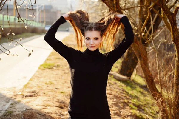 一个漂亮的年轻女孩在公园里的公路树后笑着玩长发的画像 图为春季室外天气晴朗时的照片 — 图库照片