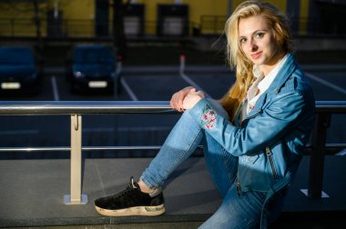 Sarışın bir kızın portresi, şehrin açık havada gün batımında, ışıkların arka planında.