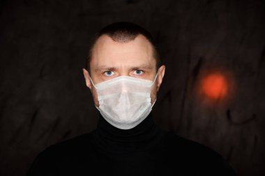Siyah arka planda kırmızı ışığı olan tıbbi maskeli beyaz bir adam.