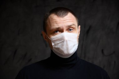 Siyah arka planda kırmızı ışığı olan tıbbi maskeli beyaz bir adam.