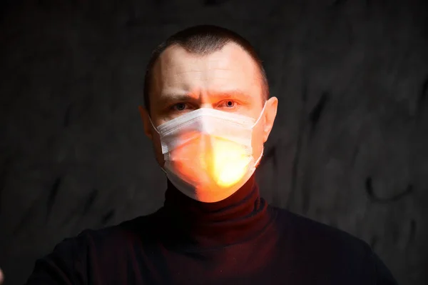 Photo Caucasian man in a medical mask with a red light on a black background