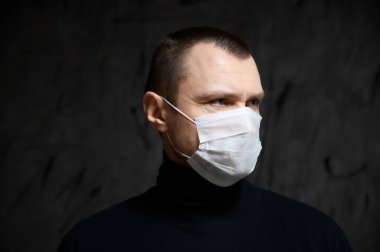 Coronavirus koruma konsepti. Siyah arka planda maskeli bir adamın fotoğrafı başka yöne bakıyor.