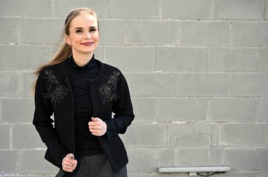 Sarışın, beyaz bir kadının, açık havada, arka planda gri bir duvarda çekilmiş bir fotoğrafı. Gülümseyen ve zevk veren modaya uygun bir model..