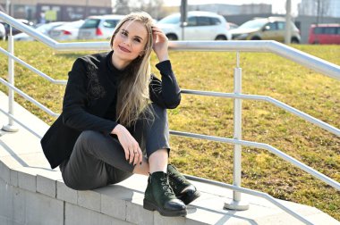 Merdivenlerin korkuluklarında gülümseyerek poz veren bir model. Açık havada güneşli bir günde genç sarışın beyaz bir kadının portresi..