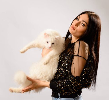 Beyaz bir arka planda beyaz bir arka planda, elinde beyaz bir kediyle şık makyajlı, esmer bir kadının portresi.