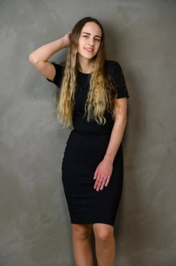 Gri arka planda dikey stüdyo fotoğrafı. Uzun saçlı, siyah elbiseli, beyaz bir kız.