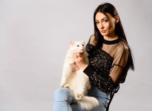 Portrait of caucasian brunette girl model on a white background in studio. Model is sitting on a chair with a white cat in her arms.