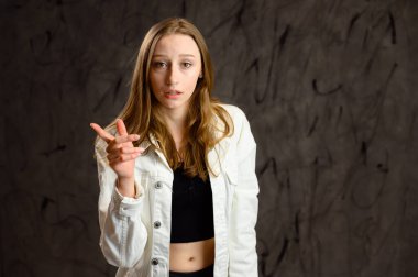 Model konuşuyor, duygularını gösteriyor. Beyaz ceketli mutlu beyaz bir kızın stüdyo fotoğrafı gri arka planda kameranın önünde duruyor..