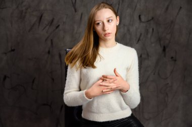 Beyaz saçlı şirin bir kızın stüdyo portresi. Gri bir arka planda, duyguları olan bir sandalyede poz veren model..