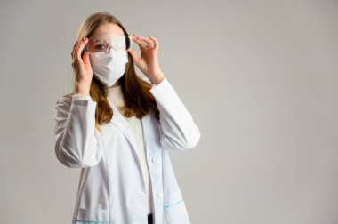Beyaz önlüklü ve gözlüklü sarışın güzel bir doktorun stüdyo portresi. Beyaz arka planda bir kadın var..