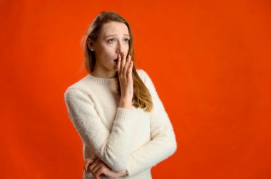 Model konuşuyor, farklı duygular gösteriyor. Stüdyo fotoğrafı beyaz kazaklı beyaz bir kızın kırmızı arka planda kameranın önünde duruşu..