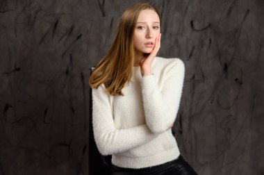 Beyaz saçlı şirin bir kızın stüdyo portresi. Gri bir arka planda, duyguları olan bir sandalyede poz veren model..