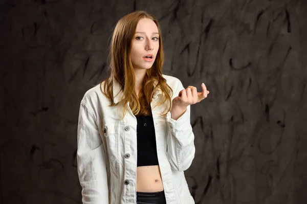模特儿在说话 流露感情 一个穿着白色夹克的快乐的高加索女孩站在相机前灰色背景的工作室照片 — 图库照片