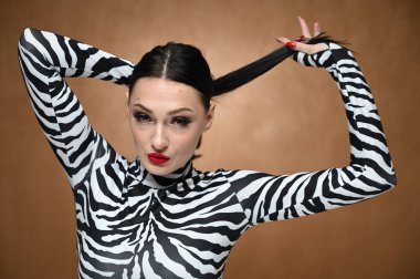 Stüdyoda bej arka planda çizgili bluz giyen, saçını elinde tutan genç bir model. Çekici beyaz bir esmerin yatay portresi..