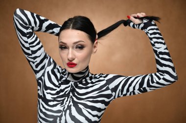 Stüdyoda bej arka planda çizgili bluz giyen, saçını elinde tutan genç bir model. Çekici beyaz bir esmerin yatay portresi..