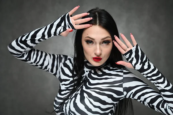 Glamorous girl in a striped blouse on a gray background in the studio. A horizontal portrait of a fashionable caucasian brunette with excellent make-up demonstrates her face.