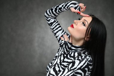 Makyajlı, beyaz tenli, şık bir esmerin yatay portresi. Stüdyoda gri arka planda çizgili bluz giyen çekici bir kız. Yan görünüm