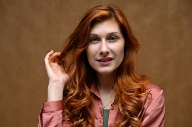 Yakın plan portre, uzun kızıl saçlı güzel bir kadının gülümsemesi. Fotoğraf, stüdyoda bej bir arkaplanda çekildi..