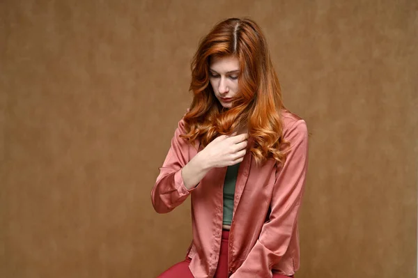 ピンクのブラウスに長い赤い髪の女性の水平方向の肖像画 ベージュ地にスタジオで撮影された写真 — ストック写真