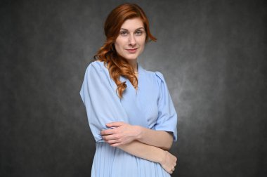 Stüdyoda gülümseyen gri bir arka planda poz veren kız model. Mavi bluzlu, kızıl saçlı güzel bir kadının portresi..