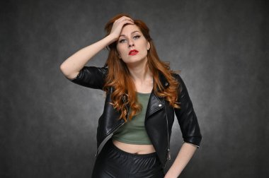 Siyah ceketli ve yeşil tişörtlü kızıl saçlı genç bir kadının yatay portresi. Stüdyonun gri arka planında mükemmel makyajlı bir model..