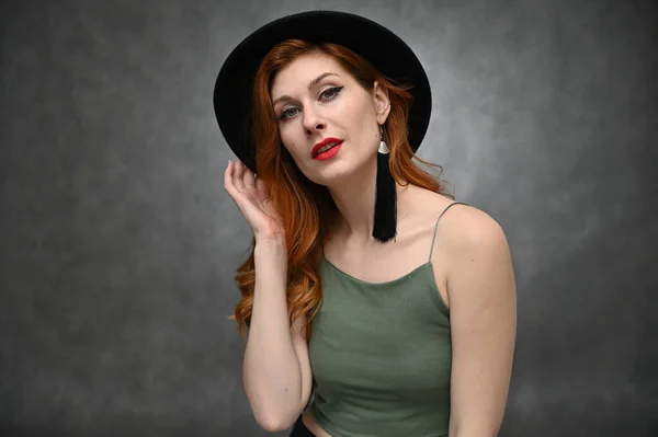 スタジオで緑のTシャツに身を包んだ素晴らしいメイクの帽子のモデル かなり赤い髪の若い女性の灰色の背景の肖像画 — ストック写真