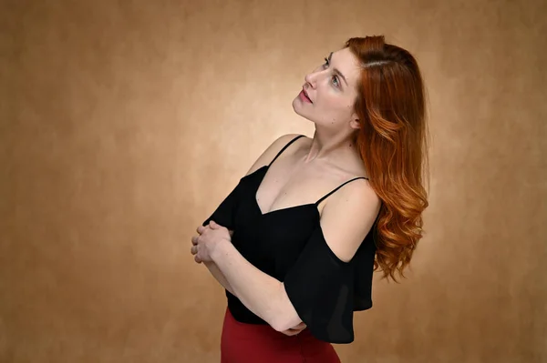 女の子モデルはベージュの背景にスタジオでポーズ 黒のブラウスにかなり赤い髪の若い女性の肖像画 — ストック写真