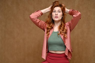 Pembe bluzlu, uzun kızıl saçlı bir kadının yatay portresi. Fotoğraf, stüdyoda bej bir arka planda çekildi..