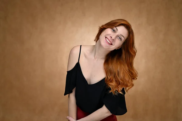 女の子モデルはベージュの背景にスタジオでポーズ 黒のブラウスにかなり赤い髪の若い女性の肖像画 — ストック写真