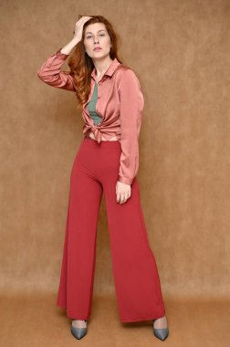 Kırmızı pantolon ve pembe bluz giymiş güzel bir manken. Çeşitli pozlarda bej arka planda beyaz saçlı genç bir kadının tam boy dikey portresi..