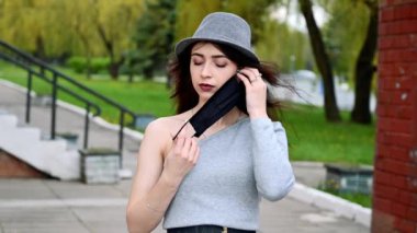 Güzel, gülümseyen esmer bir kızın video portresi. Şehir parkında bir sağlık maskesini takıyor.