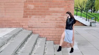 Güzel, gülümseyen esmer bir kızın video portresi şehirdeki bir binaya karşı üst kata çıktı.