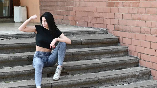 街の通りに建物の階段の背景にポーズをとる優れたメイクと写真フィットネスブルネットの女の子 — ストック写真