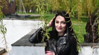 Mükemmel makyajlı esmer bir kızın portresi. Arka planda ağaç dallarında poz veriyor. Sokakta gülümsüyor..