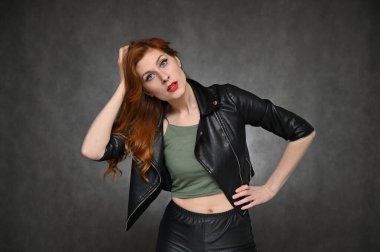 Model pozları değiştirerek farklı duyguları gösteriyor. Yeşil tişörtlü ve gri arka planda siyah ceketli güzel kızıl saçlı bir kadının portresi..