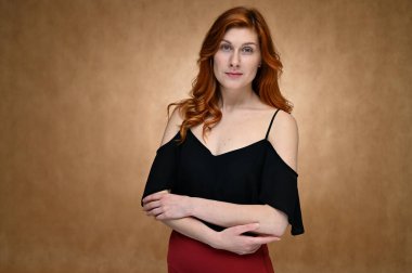 Siyah bluz giymiş güzel kızıl saçlı genç bir kadının portresi. Stüdyoda bej arka planda poz veren bir model..