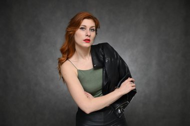 Model pozları değiştirerek farklı duyguları gösteriyor. Yeşil tişörtlü ve gri arka planda siyah ceketli güzel kızıl saçlı bir kadının portresi..