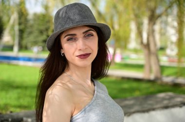 Bahar parkında gülümseyerek poz veren bir model. Beyaz saçlı, gri elbiseli, siyah şapkalı, değişik pozlarda bir kızın yakın plan portresi..